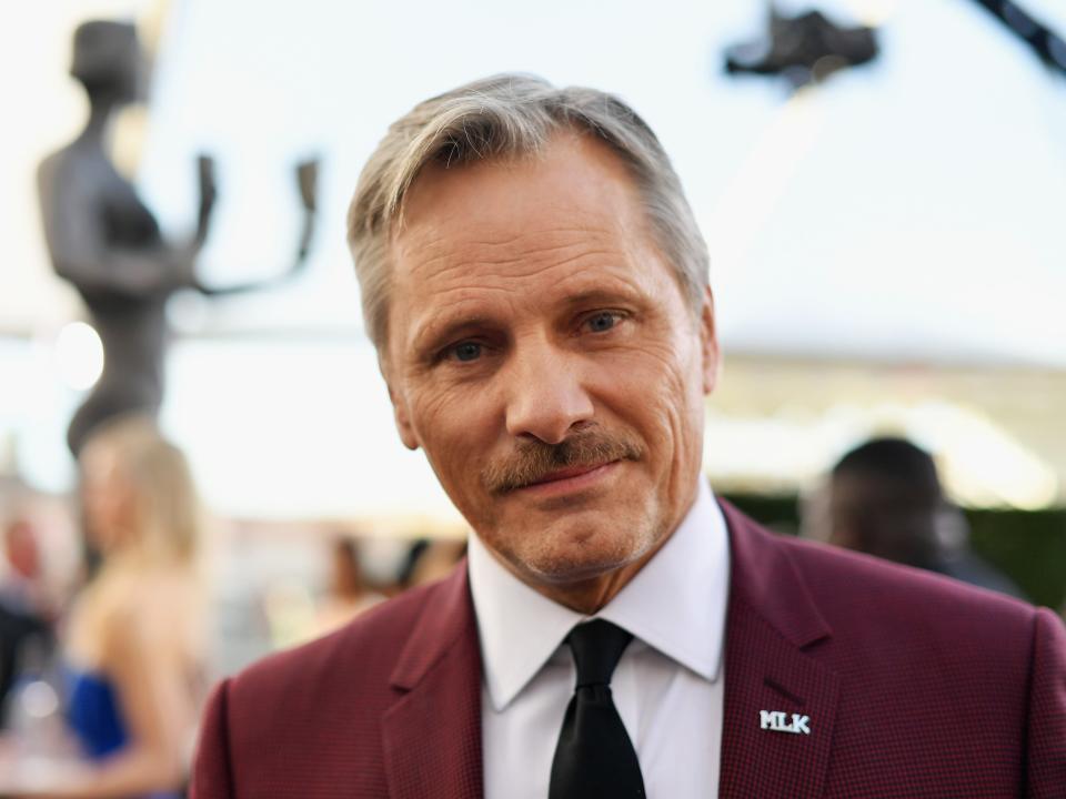 Viggo Mortensen wearing a red suit and white button down at a red carpet event