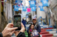 A couple has a photo taken in front of banners and writings in support of Napoli soccer team, in downtown Naples, Italy, Tuesday, April 18, 2023. It's a celebration more than 30 years in the making, and historically superstitious Napoli fans are already painting the city blue in anticipation of the team's first Italian league title since the days when Diego Maradona played for the club. (AP Photo/Andrew Medichini)