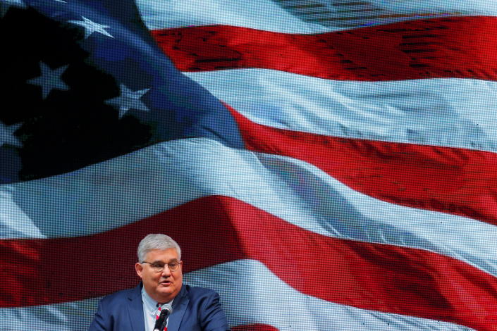 David Shafer frente a una enorme imagen de una bandera estadounidense ondeando.