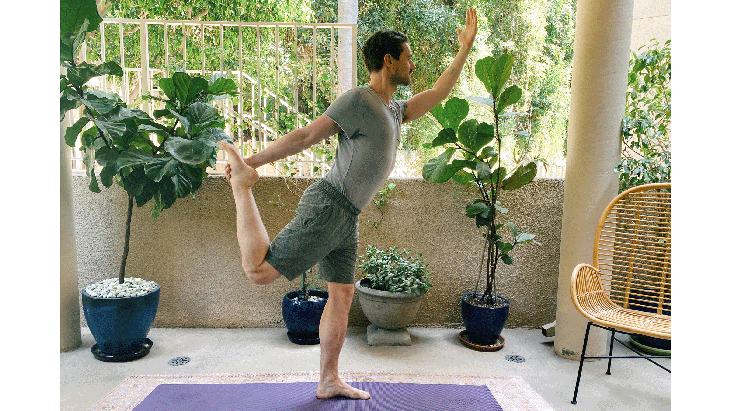 Man standing on a rug balancing on one leg and practicing yoga