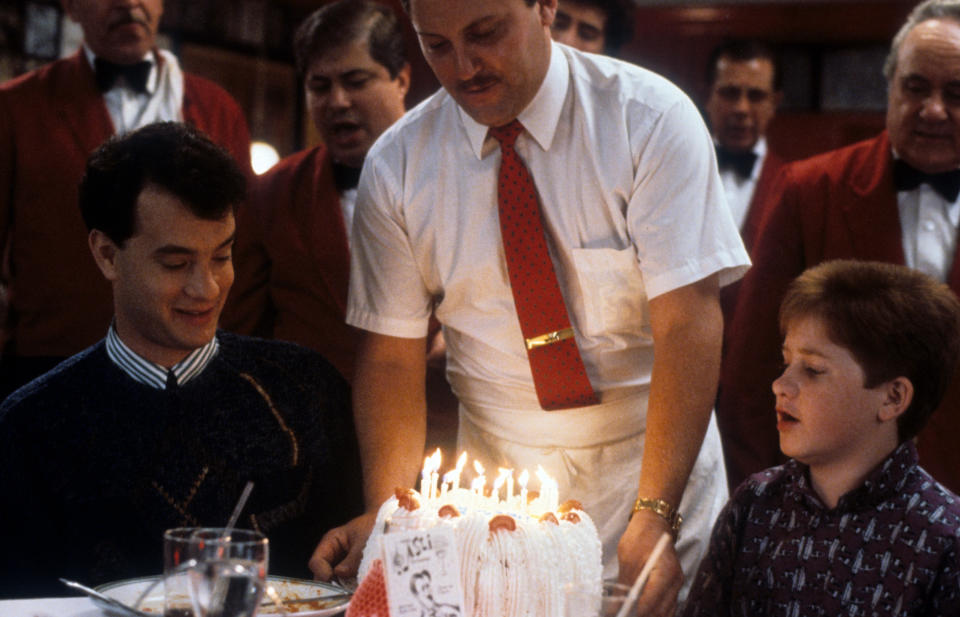 Tom Hanks sentado en una mesa de comedor con un niño mientras les entregan un pastel de cumpleaños en una escena de la película 'Big', 1988. (Foto de 20th Century-Fox/Getty Images)