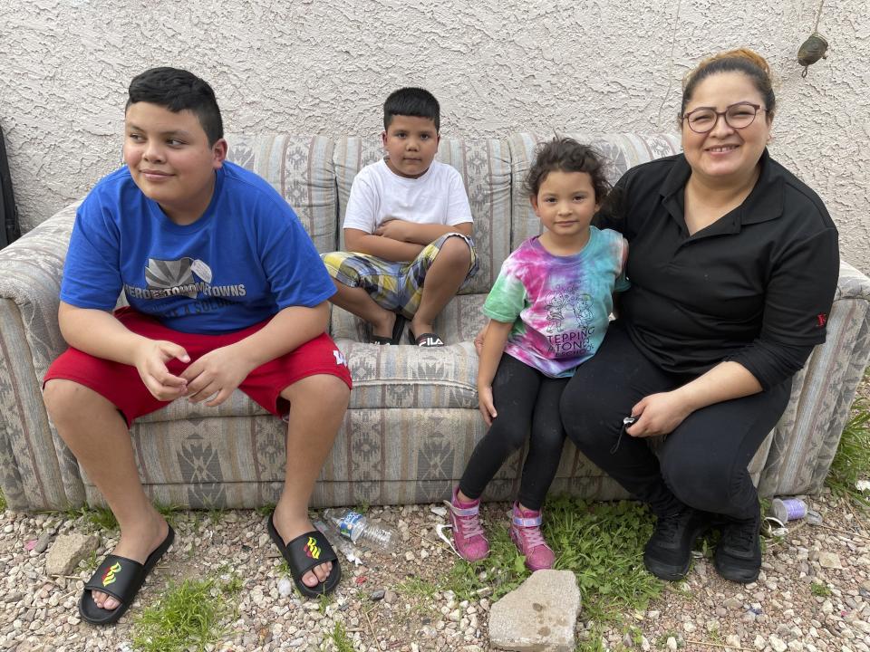 Silvia Baca Garcia, 33, sits outside her home she shares with her three children and two grandchildren in Phoenix, on Thursday, March 25, 2021. From left are her sons, Hugo, 14, and Adrian, 6, and granddaughter, Sofia. Originally from Honduras, Baca Garcia says she struggled to feed her family when she was out of work for months during the coronavirus pandemic. She said she's relieved that her two school-aged sons are now back on campus, where they each get two hot meals every day they go to class. (AP Photo/Anita Snow)