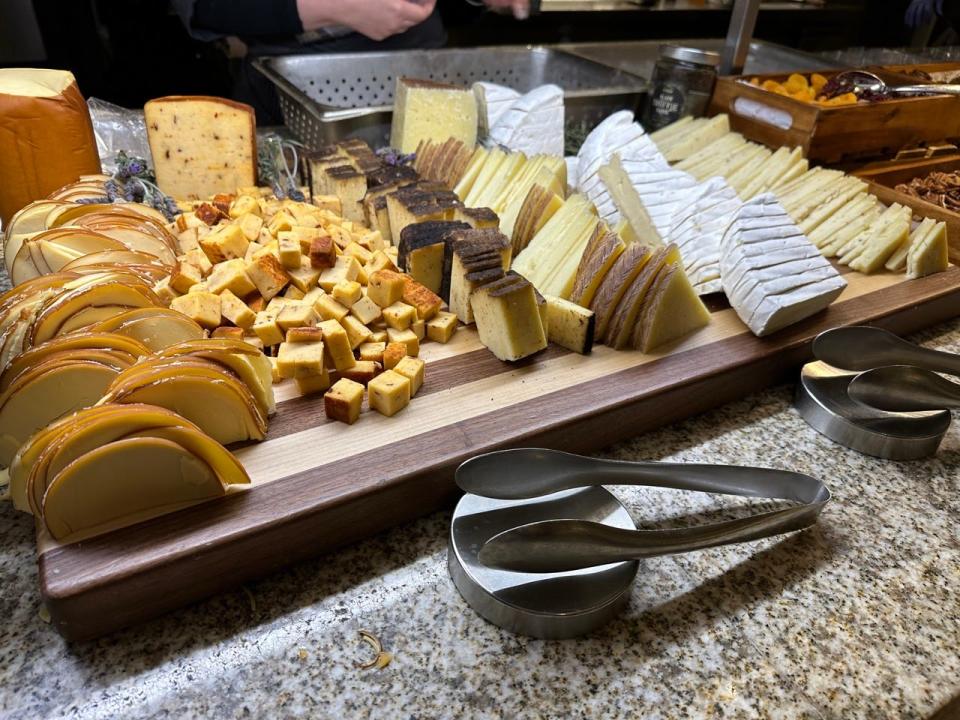 Stacks of cheeses on wooding cutting board with tongs in front if it at Bacchanal buffet