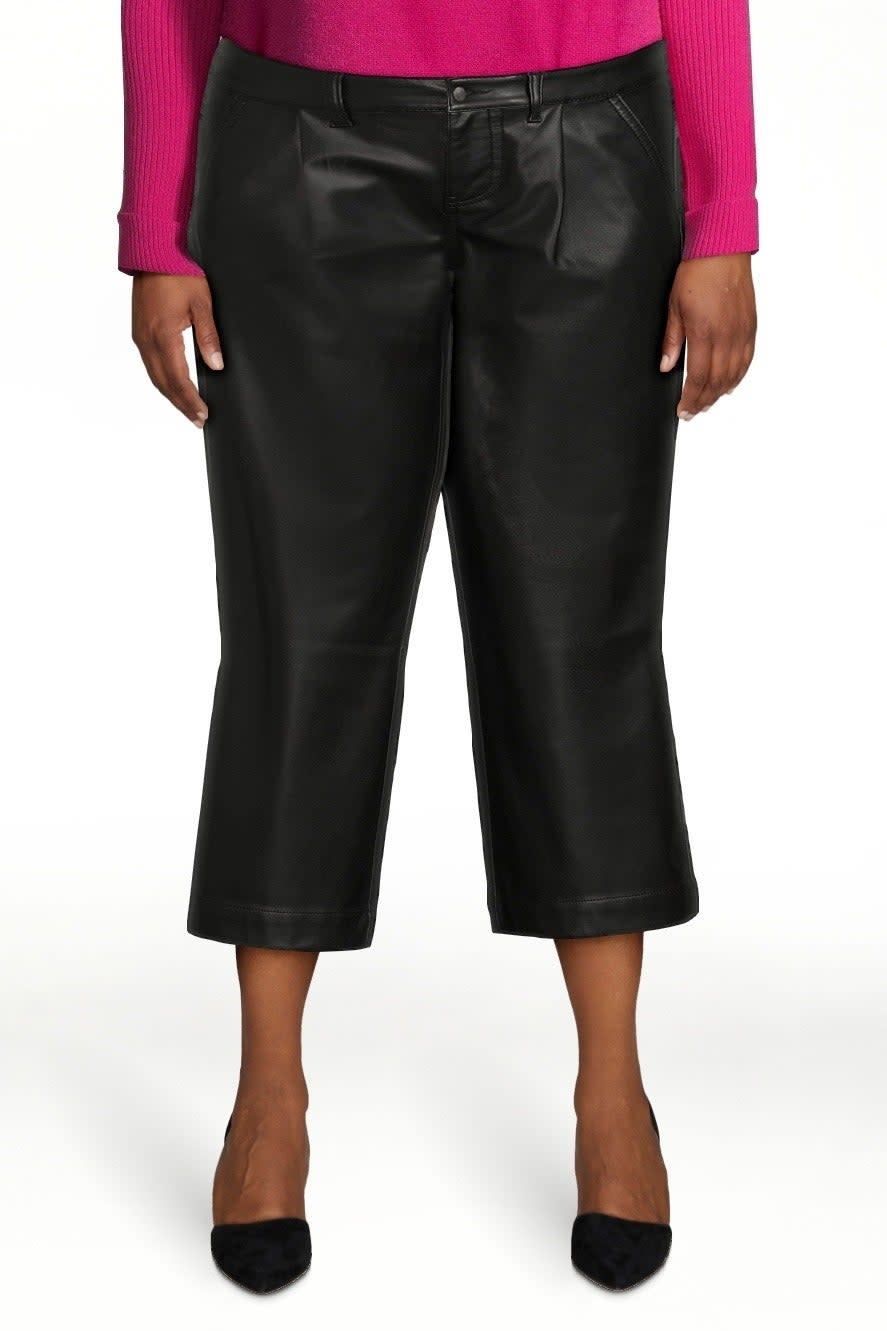 Cropped image focusing on a person wearing black leather culottes with a pink top, paired with black pointed-toe heels