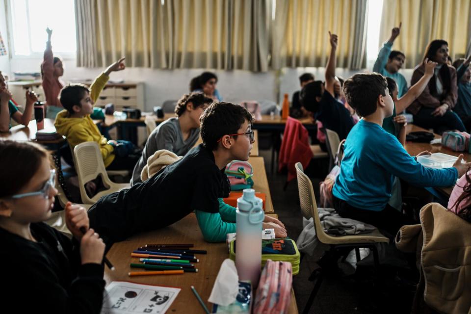 Children seated at desks in class, some with hands raised