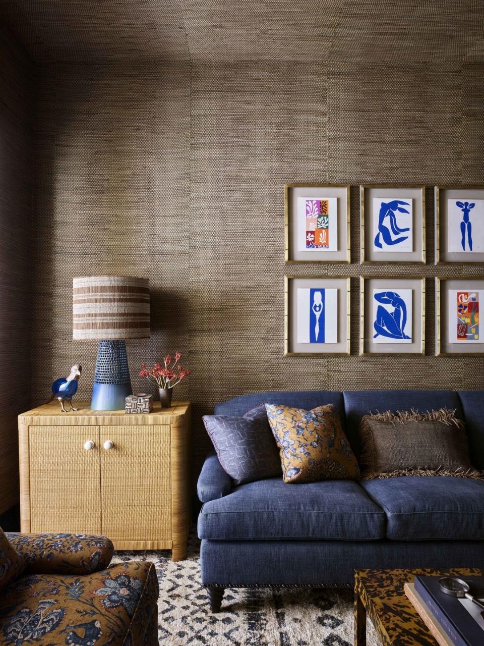 brown dried water hyacinth covered walls, blue sofa, and a grid of colorful artwork by henri matisse behind