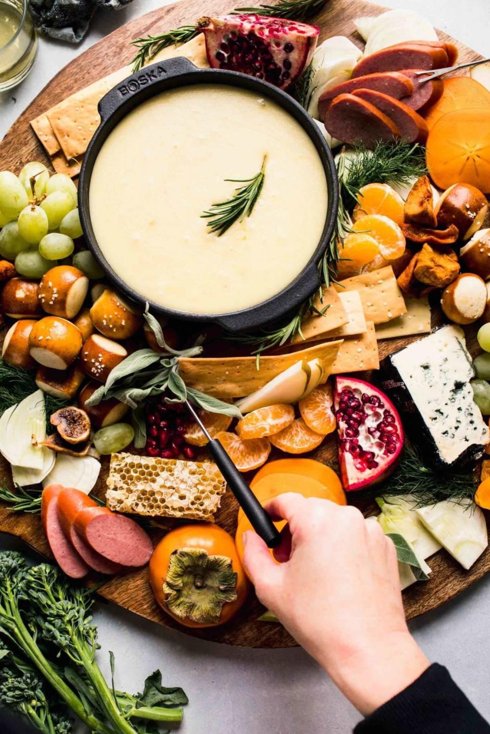 Cheese fondue with vegetables, crackers, bread, and fruit for dipping.