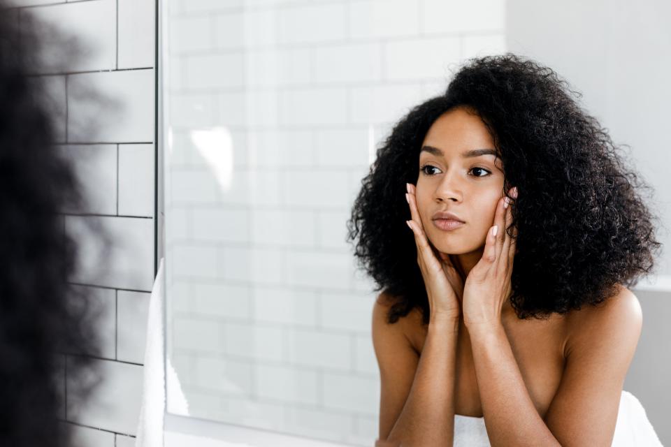 Mixed-race woman applying skincare while staring in the mirror.