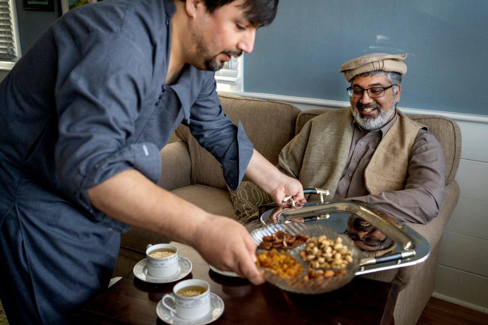 A man serves food, while another looks on, smiling.