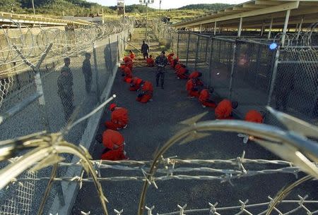 Detainees in orange jumpsuits sit in a holding area under the watchful eyes of military police during in-processing to the temporary detention facility at Camp X-Ray of Naval Base Guantanamo Bay in this January 11, 2002 file photograph. REUTERS/Stringer/Files