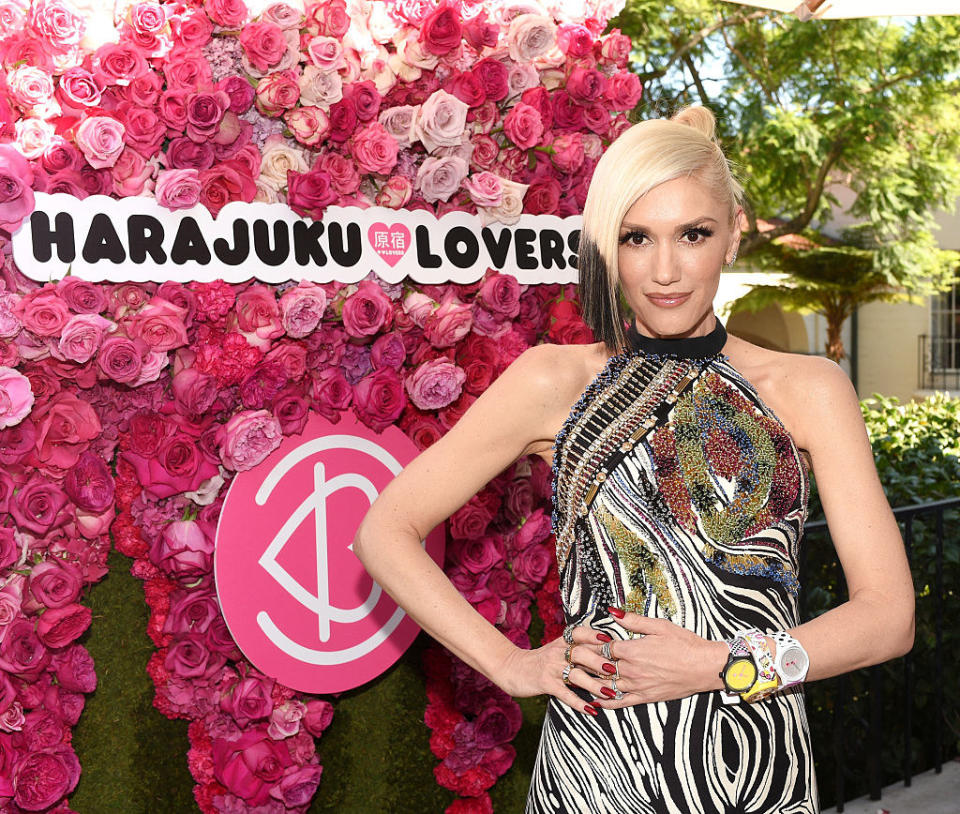 Gwen standing next to a flower wall with an attached sign that says "Harajuku Lovers"