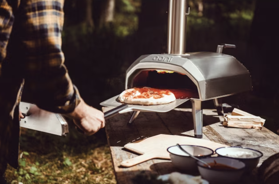 model taking pizza out of silver Ooni pizza oven