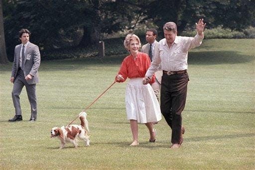 President Ronald Reagan and first lady Nancy Reagan wave as they walk with their dog Rex on the South Lawn of the White House on Sunday, June 15, 1986 in Washington after returning by helicopter from Camp David, Maryland. The Reagans spent the weekend at the presidential retreat and returned to the executive mansion on Father's Day. The man in the background is unidentified.