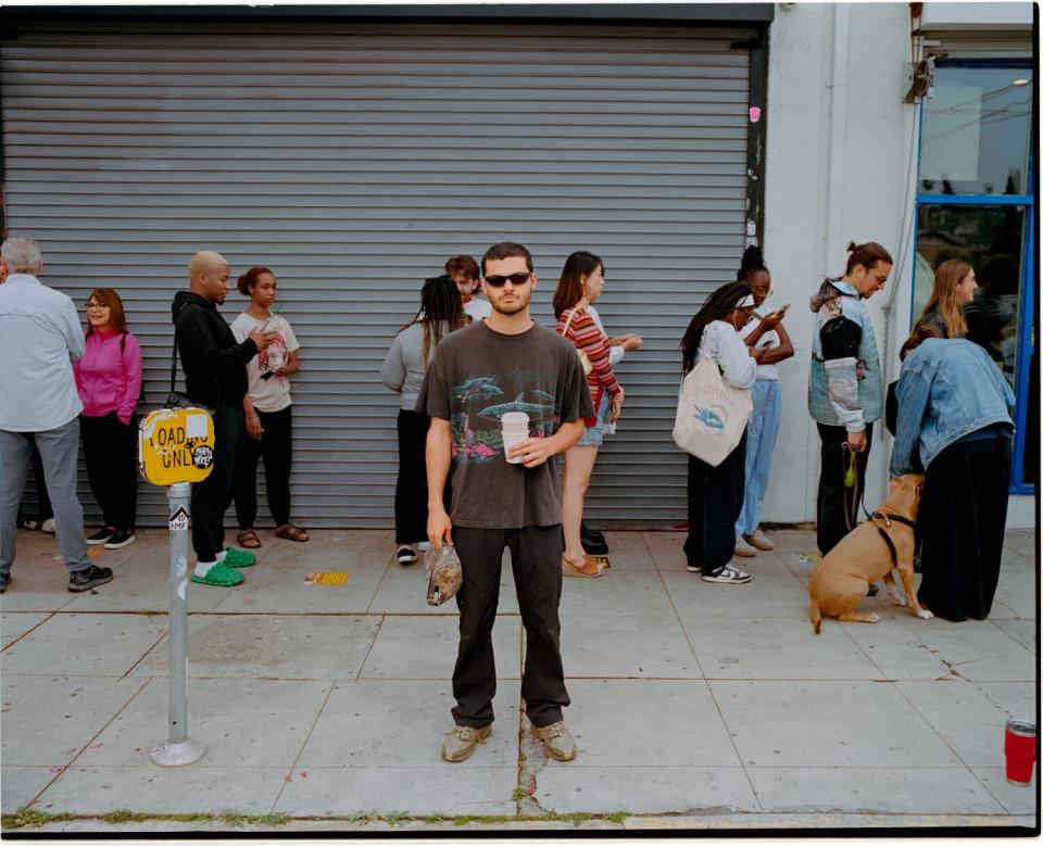 Man in brown shirt and black pants stands outside a line.