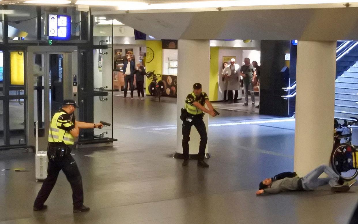 Dutch police officers point their guns at a wounded 19-year-old man who was shot by police after stabbing two people in the central railway station in Amsterdam - Tdwholesale