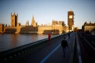 People walk on Westminster bridge in front of the Houses of Parliament, in London