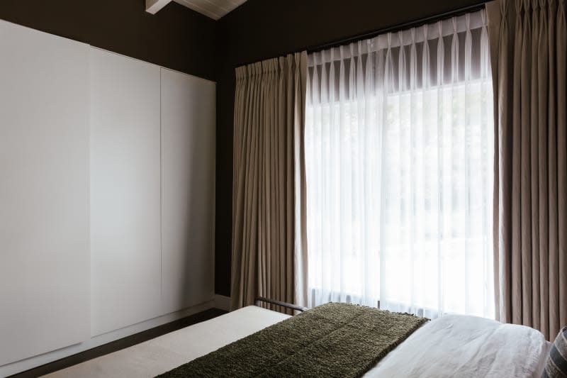 White sliding doors to closet, beige curtains, white bedding with green throw blanket