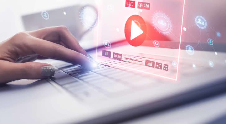 Image of a person pressing a button on a laptop and a holographic projection of a music player appearing to represent streaming stocks