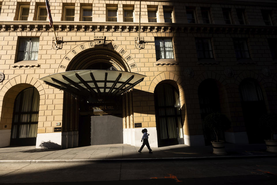 A pedestrian passes a boarded up entrance to the Omni San Francisco Hotel, which has suspended operations due to the COVID-19 pandemic, on Wednesday, Oct. 21, 2020, in San Francisco. As the coronavirus pandemic transforms San Francisco's workplace, legions of tech workers have left, able to work remotely from anywhere. Families have fled for roomy suburban homes with backyards. The exodus has pushed rents in the prohibitively expensive city to their lowest in years. (AP Photo/Noah Berger)