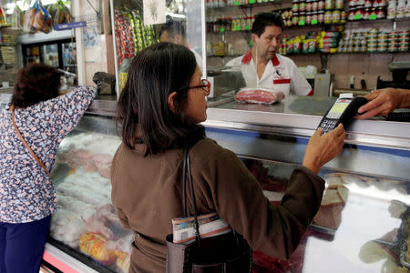 FILE PHOTO: A woman uses a PoS device to pay for her groceries at a store in downtown Caracas, Venezuela March 10, 2017. REUTERS/Marco Bello/File Photo