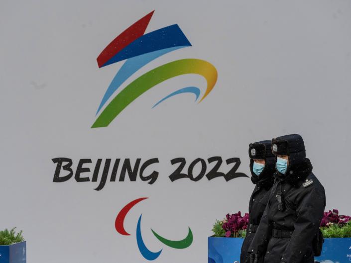 Security walk by a billboard for the Beijing 2022 Winter Olympics and Paralympics during a snowfall on January 20, 2022 in Beijing, China.