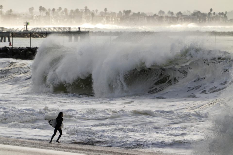 A surfer runs into the turbulent surf in Seal Beach, Calif., Saturday, Dec. 30, 2023. (AP Photo/Damian Dovarganes)