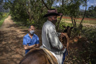 Luis Orlando Deulofeu, who owns the MogoteArt Hostel, poses for a portrait behind a passing horse rider outside his hotel in Viñales, Cuba, March 1, 2021. Both U.S. sanctions meant to punish the government and a COVID-19 pandemic have squashed tourism almost everywhere, making some Cubans hope that new U.S. President Joe Biden will reverse at least some of the restrictions implemented by his predecessor. (AP Photo/Ramon Espinosa)