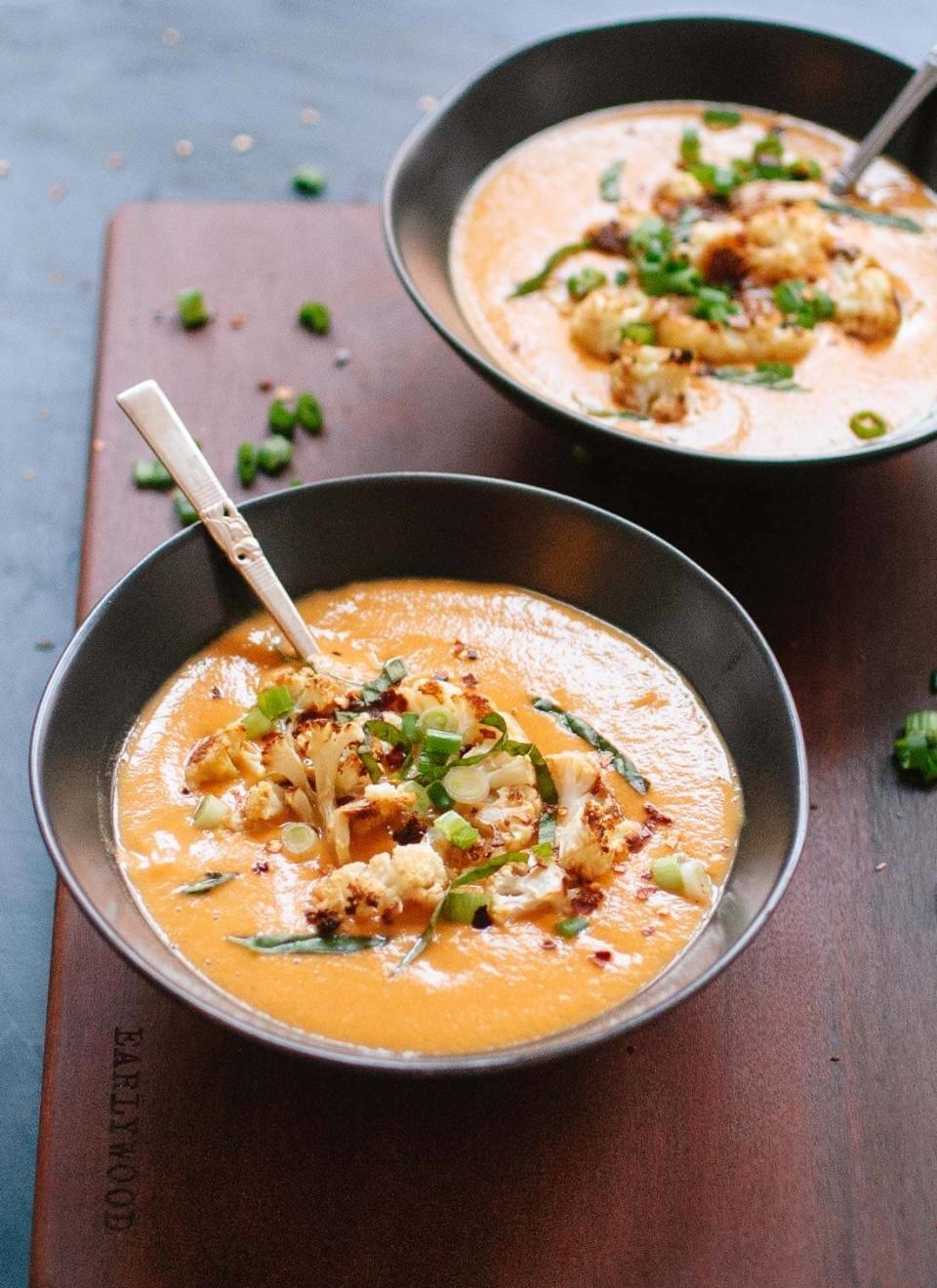 two bowls of curried cauliflower soup topped with roasted cauliflower and herbs