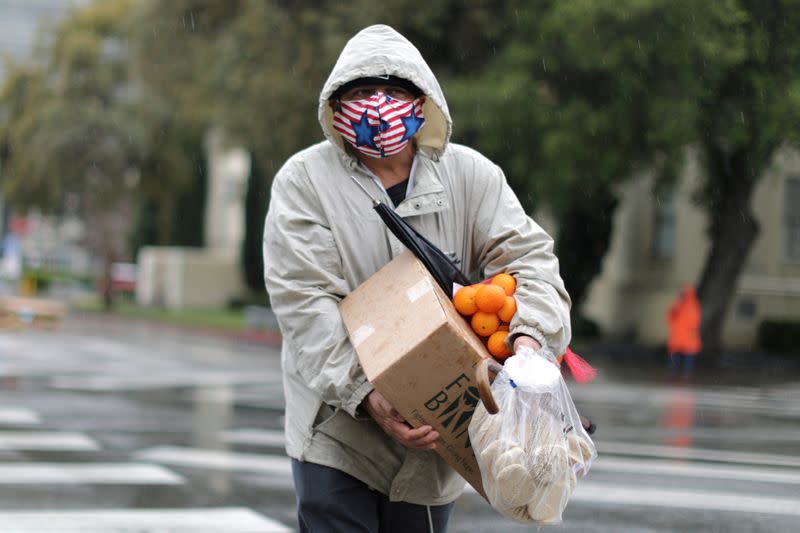 FILE PHOTO: A man carries fresh food in the rain at a Los Angeles Regional Food Bank giveaway of 2,000 boxes of groceries, as the spread of the coronavirus disease (COVID-19) continues, in Los Angeles