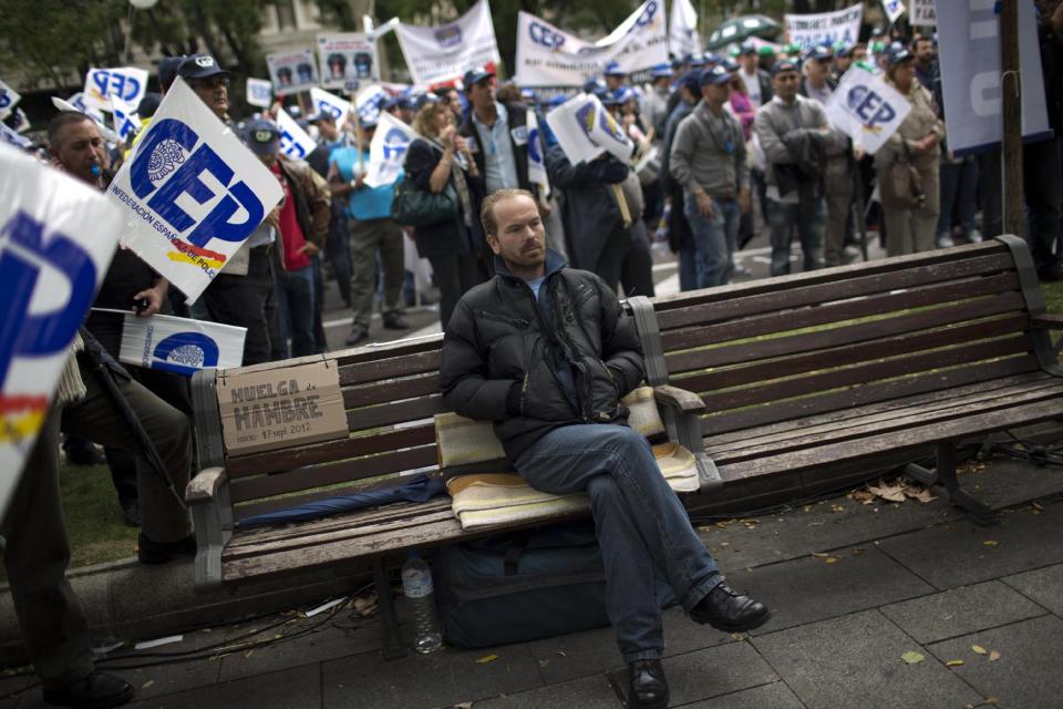 Rumanian immigrant in Spain Sorin Bedreaga, 38, sits on a bench where he says he has spent 40 days on a hunger strike, as police officers protest by blocking the street in front of the Interior Ministry in Madrid, Spain, Saturday, Oct. 27, 2012. The demonstrators were protesting the government’s austerity measures, especially the elimination of their Christmas bonus pay, one of 14 paychecks that most Spanish civil servants get each year. The placard next to Sorin reads in Spanish "Hunger strike since 17 September 2012". (AP Photo/Emilio Morenatti)