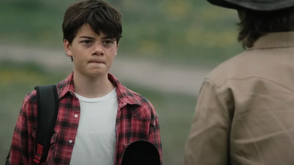 Tate in Yellowstone standing in front of a fence while talking to Kayce.