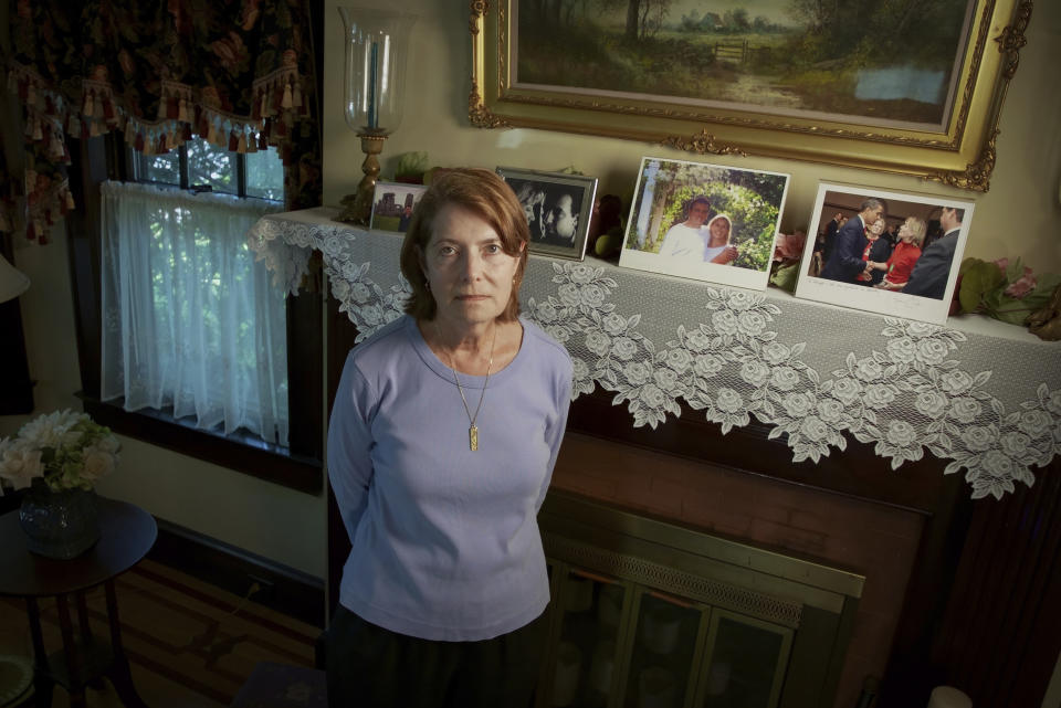 Margot Eckert stands by a display of pictures of her brother-in-law Sean Rooney and sister Beverly Eckert at her home, Thursday, July 15, 2021, in Springfield, Mass. Rooney was killed on 9/11 while working in his office in the South Tower. His wife, Beverly, died in a plane crash in 2009. The collection of some 22,000 personal artifacts — some on display at the 9/11 museum, and others on display at other museums around the country — provide a mosaic of lost lives and stories of survival: wallets, passports, baseball gloves, shoes, clothes and rings. (AP Photo/Robert Bumsted)