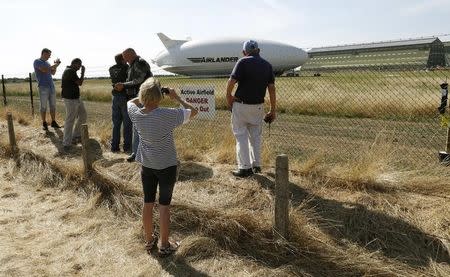 People look through the perimeter fence at the Airlander 10 hybrid airship following a crash-landing during a test flight at Cardington Airfield in Britain, August 24, 2016. REUTERS/Darren Staples