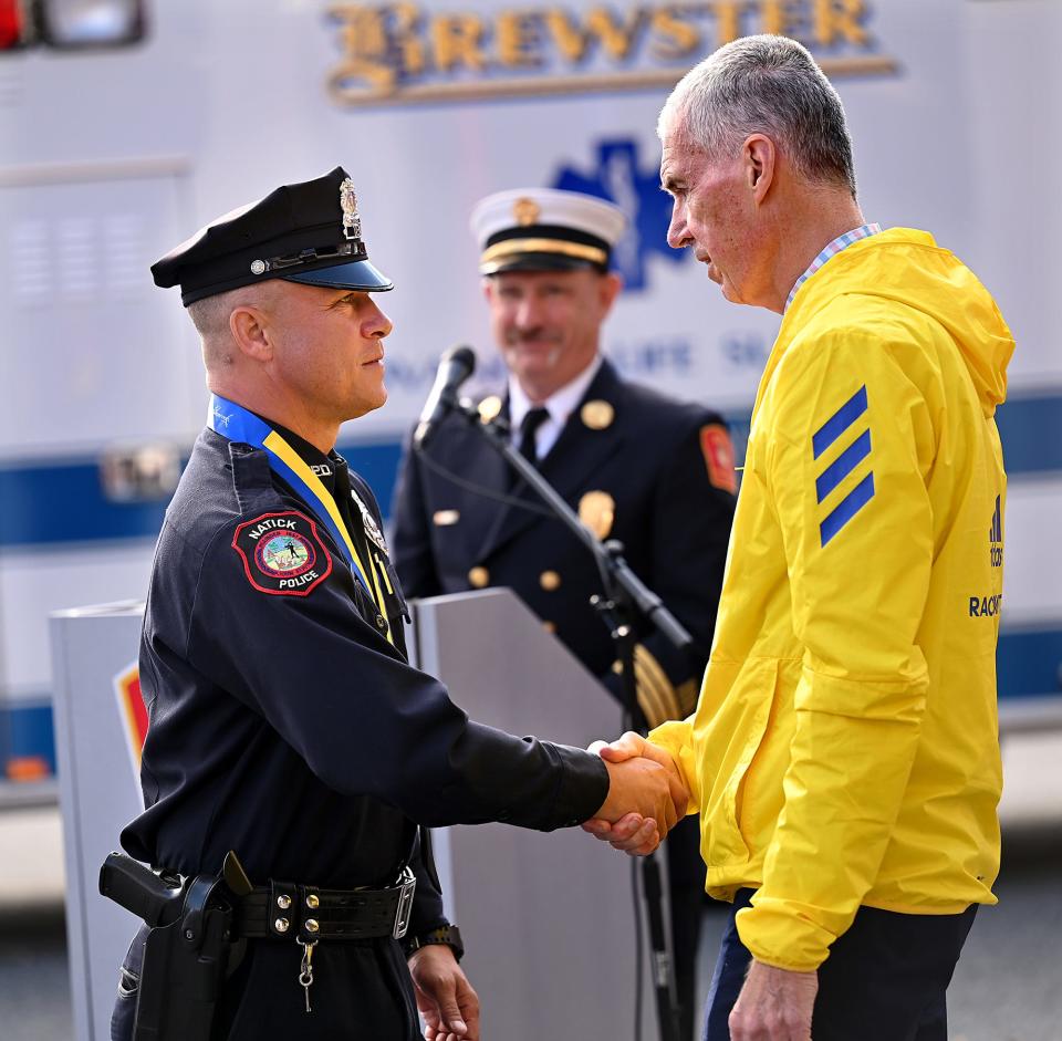 Natick Police Officer Scott Wade, left, shakes hands with Tom Grilk, President and CEO of the Boston Athletic Association, after receiving an honorary medal for helping a stricken runner at last month's Boston Marathon, during a ceremony at Natick Fire Headquarters, Nov. 10, 2021.  Nine first responders were recognized Wednesday for providing immediate life-saving car for professional runner Meghan Roth, 34, of Minneapolis, Minnesota, who suffered a cardiac episode in Natick near the Framingham line on Marathon day, Oct. 11, 2021.  