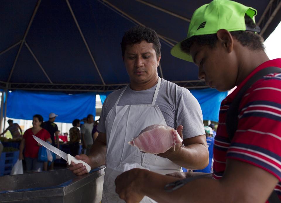 Villager Edson de Souza (L) from the Rumao Island community, sells part of his catch of arapaima or pirarucu, the largest freshwater fish species in South America and one of the largest in the world, after fishing in a branch of the Solimoes river, one of the main tributaries of the Amazon, at a market near Fonte Boa, about 600 km (373 miles) west of Manaus, November 30, 2013. Catching the arapaima, a fish that is sought after for its meat and is considered by biologists to be a living fossil, is only allowed once a year by Brazil's environmental protection agency. The minimum size allowed for a fisherman to keep an arapaima is 1.5 meters (4.9 feet). Picture taken November 30, 2013. REUTERS/Bruno Kelly (BRAZIL - Tags: ENVIRONMENT SOCIETY ANIMALS) ATTENTION EDITORS: PICTURE 19 OF 22 FOR PACKAGE 'FISHING FOR BRAZIL'S FOSSILS'. TO FIND ALL IMAGES SEARCH 'ARAPAIMA KELLY'