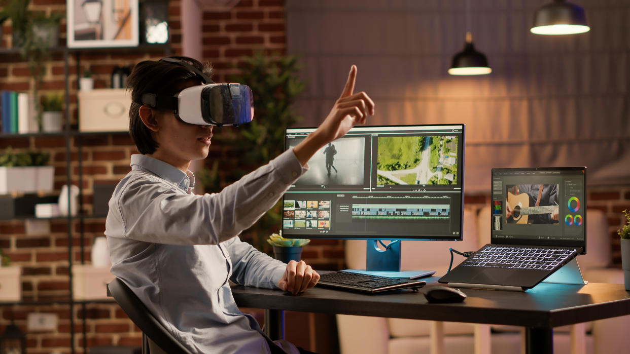  A woman with a VR headset on in front of a suite of video editing software . 