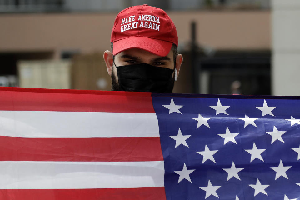 Sevag Demirjian, a supporter of President Trump, waves an American flag at passing demonstrators during a protest outside of the Edward R. Roybal Federal building Tuesday, March 31, 2020, in Los Angeles. Demonstrators across California coordinated efforts in a car-based protest to demand the release of immigrants in California detention centers over concerns over the COVID-19 pandemic. (AP Photo/Marcio Jose Sanchez)
