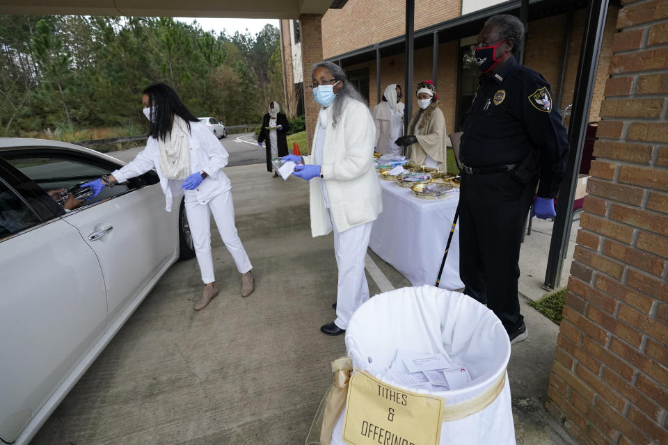 Ushers prepare collect offerings, distribute communion packets and distribute some personal protection products to members arriving for the First Sunday service at Anderson United Methodist Church, Sunday, Dec. 6, 2020, in Jackson, Miss. The church has taken to using digital means by which to broadcast each worship service to its members . However, the congregants gather in their vehicles in the church's parking lot to celebrate the receiving of communion. (AP Photo/Rogelio V. Solis)