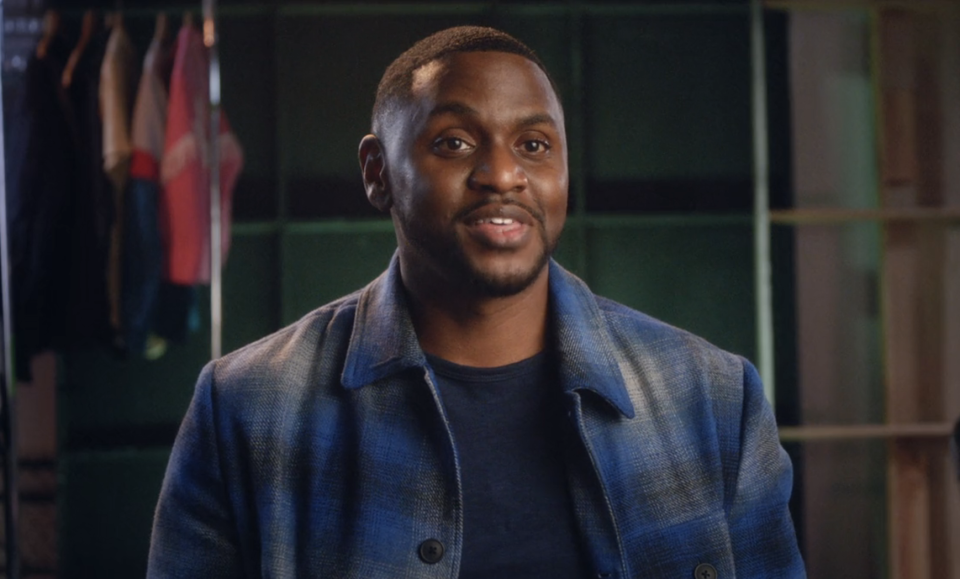 Leon in a denim jacket smiling in an interview setting with a blurred clothing rack in the background