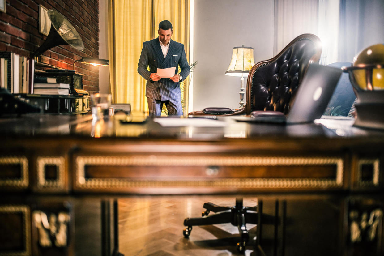 Businessman reading documents and uses the phone and computer in the office (zeljkosantrac / Getty Images)