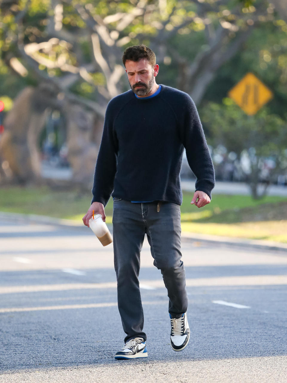 he's looking down while he walks and holds an almost empty iced coffee