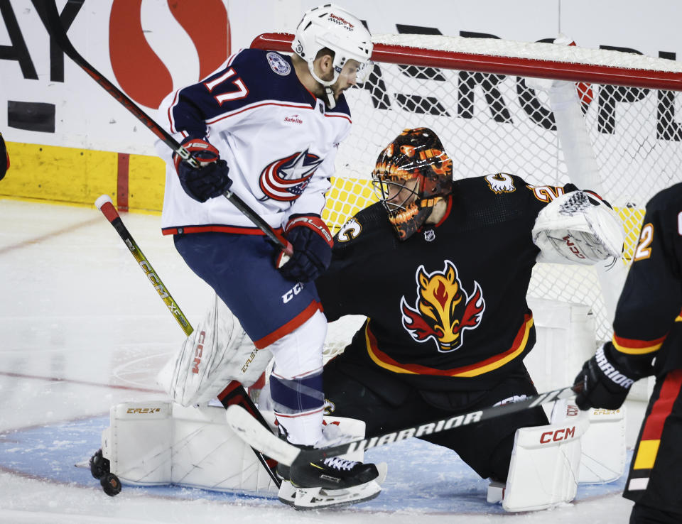 Columbus Blue Jackets forward Justin Danforth (17) tries to get out of the way of a teammate's shot as Calgary Flames goalie Jacob Markstrom (25) kicks it away during the third period of an NHL hockey game Thursday, Jan. 25, 2024, in Calgary, Alberta. (Jeff McIntosh/The Canadian Press via AP)