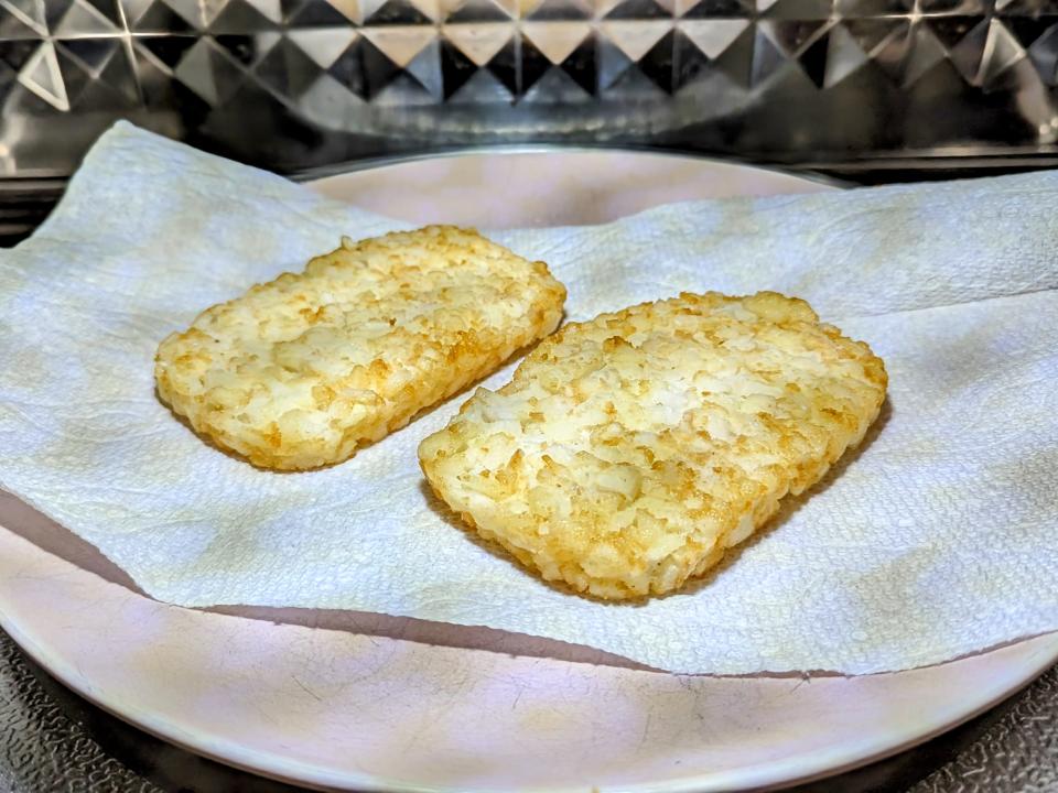 two frozen hash brown patties on a plate in the microwave