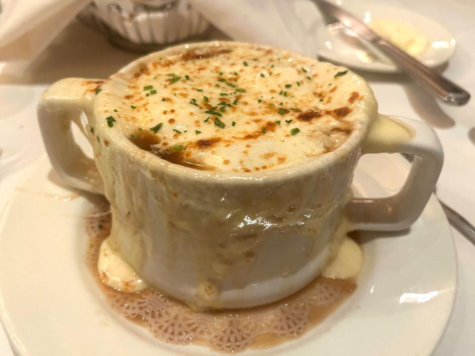 A large cup of French onion soup, with cheese and broth dripping over the sides of the cup.