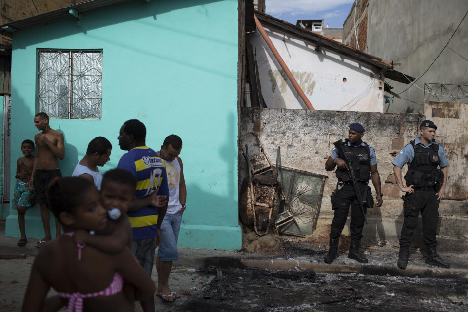 Police officers, right, stand guard among burned remains of a car from the Pacifying Police Unit post at the Mandela shantytown, part of the Manguinhos slum complex, in Rio de Janeiro, Brazil, Friday, March 21, 2014. Rio de Janeiro police say suspected drug gang members on Thursday night attacked three police slum outposts and burned one of them. Officials say they'll ask for elite Brazilian federal police to help quell a wave of violence in supposedly pacified slums. (AP Photo/Felipe Dana)