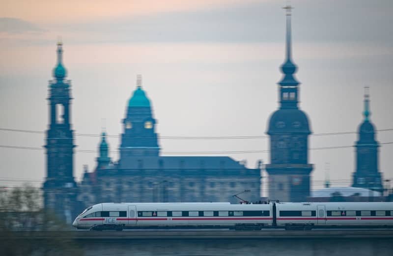 A Deutsche Bahn ICE train crosses the Marienbruecke bridge in the morning against the backdrop of the old town. Robert Michael/dpa
