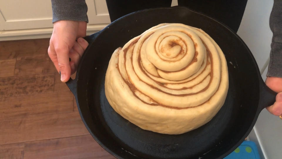In this April 11, 2020 image from video provided by Whitney Rutz, Whitney Rutz displays a large cinnamon roll before putting it in the oven in her home in Portland, Ore. Rutz baked cinnamon rolls to help raise funds for Oregon Food Bank. (Whitney Rutz via AP)