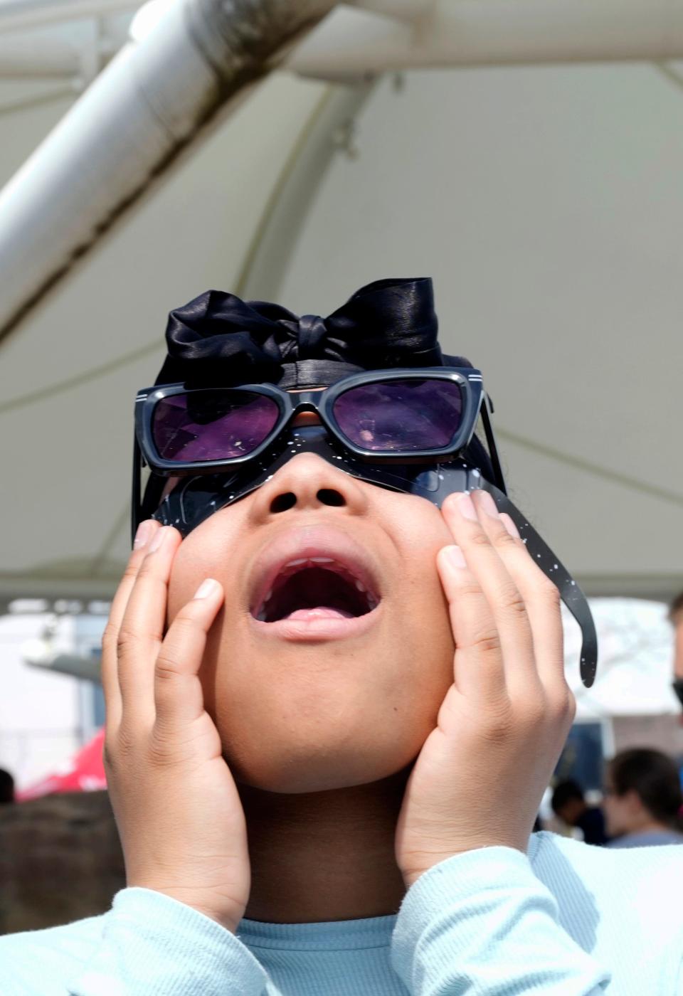 Janasia Moore, 10, of Staten Island, New York, looks through her eclipse glasses, Monday, April 8, 2024, at Liberty Science Center, in Jersey City.