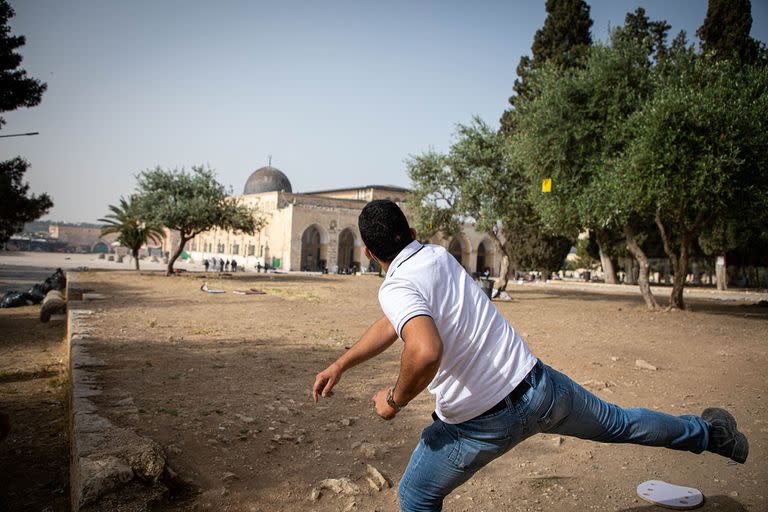 Un palestino lanza una piedra contra la policía israelí que utiliza gas lacrimógeno, balas de goma y granadas de aturdimiento para dispersar manifestantes palestinos que custodiaban la Mezquita de Al-Aqsa, Jerusalén 