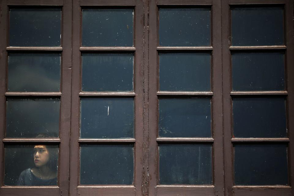 A person looks through the window onto the street where police and anti-government protesters clash near the Government House in Bangkok